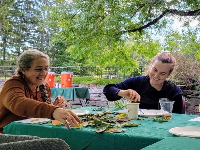 Two park visitors sit at a table outdoors and paint with real leaves as a guideVisitors enjoy painting with watercolor 