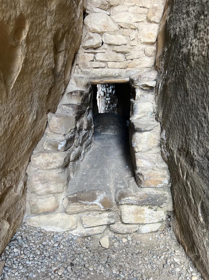A small stone-lined tunnel goes between two sandstone rock faces.The entrance to an 18 inch wide, 12 foot long tunnel in Balcony House passes through a natural crack in the rock cliff.