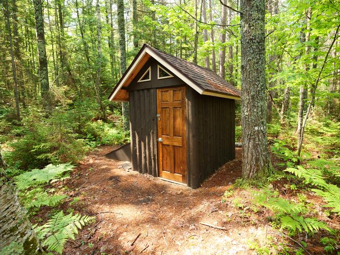 Primitive log-cabin toilet, surrounded by tall trees in the forest.