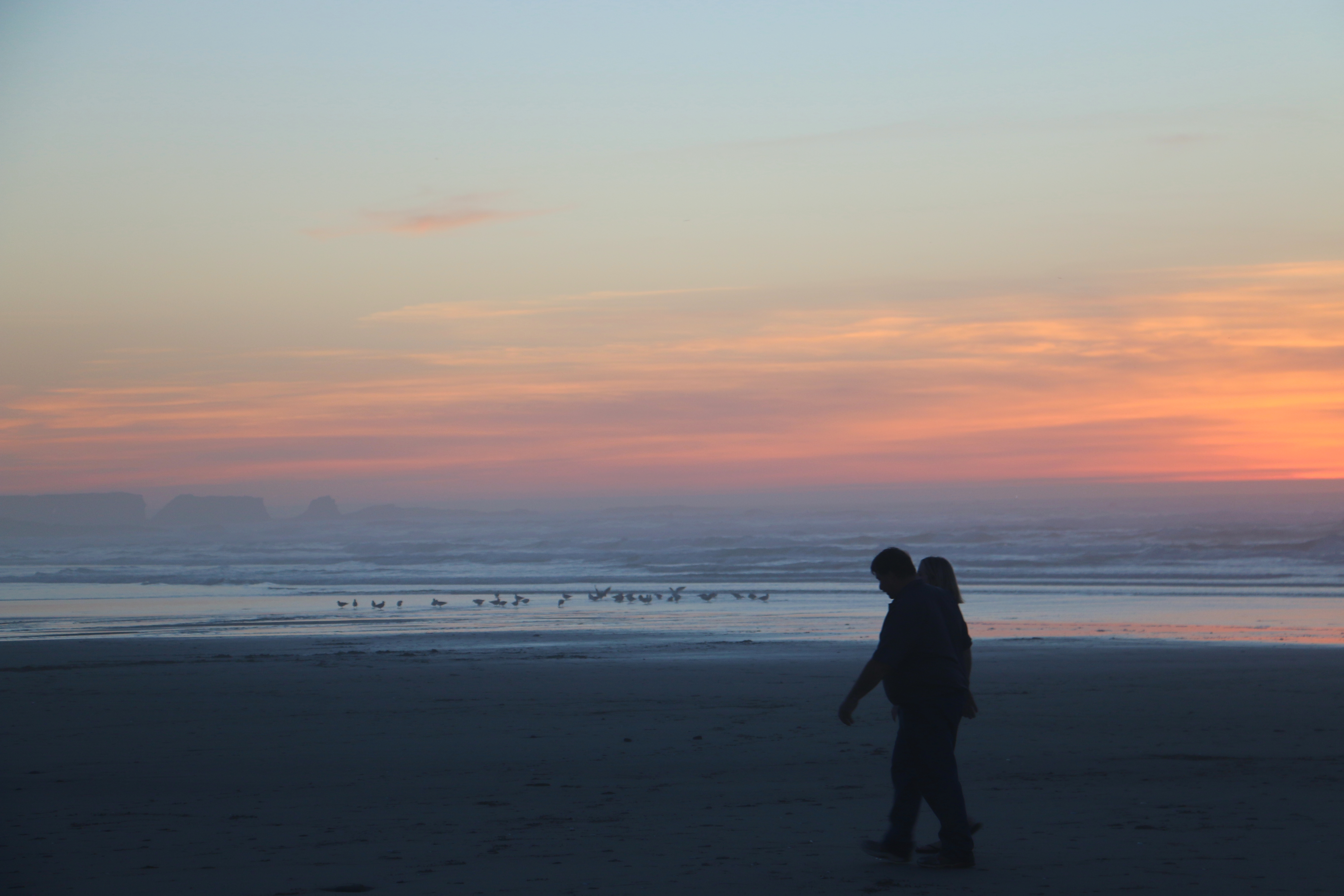 Two people walk across Bastendorff Beach at sunset.