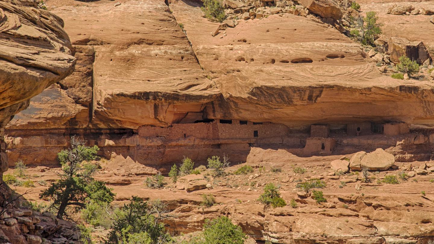 A substantial rock and mortar structure with rectangular windows and doors is sandwiched into a seam of a large sandstone cliff.Moon House is one of the most spectacular archeological sites on Cedar Mesa; a permit is required to visit this site.