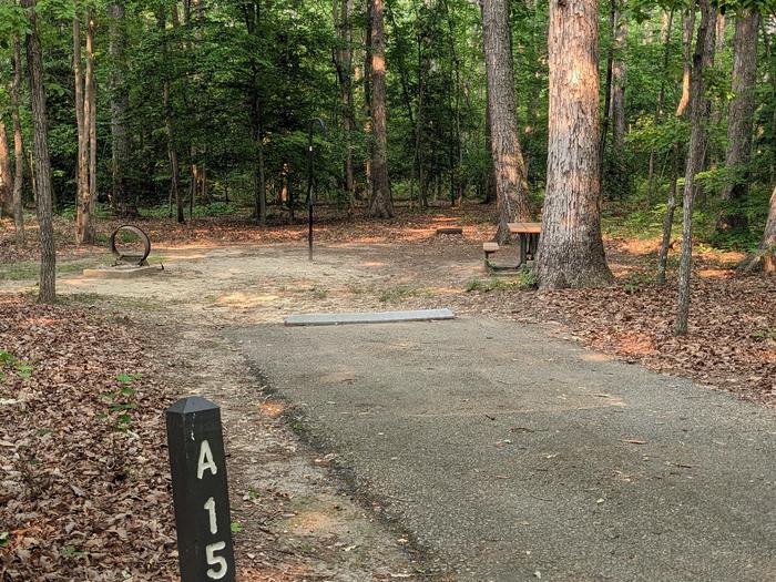 Paved parking space, picnic table, and fire ring in a shaded forest campsiteCampsite A15