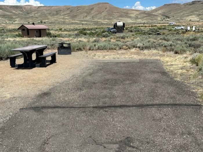 Campsite 18: driveway, picnic table, and firepit. Set in sagebrush with view of vault toilet.Loop A Campsite 18: driveway, picnic table, and firepit.