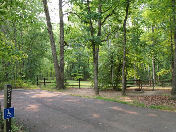 Wide paved handicapped parking space, picnic table, and fire ring in a shaded forest campsiteCampsite B25