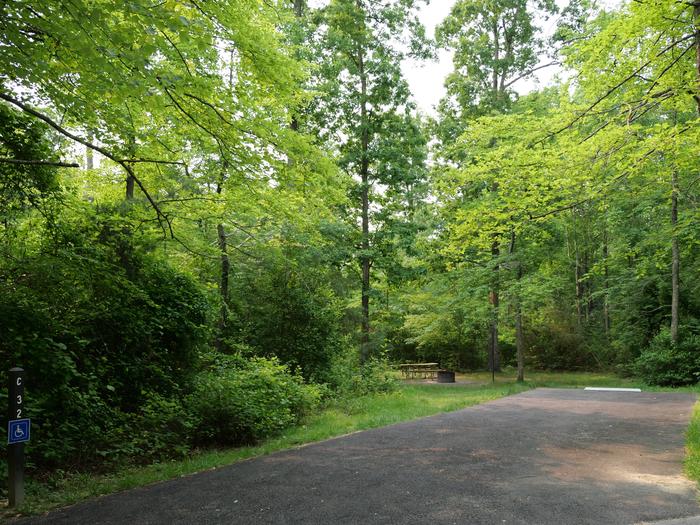 Wide paved handicapped parking space, picnic table, and fire ring in a shaded forest campsiteCampsite C32