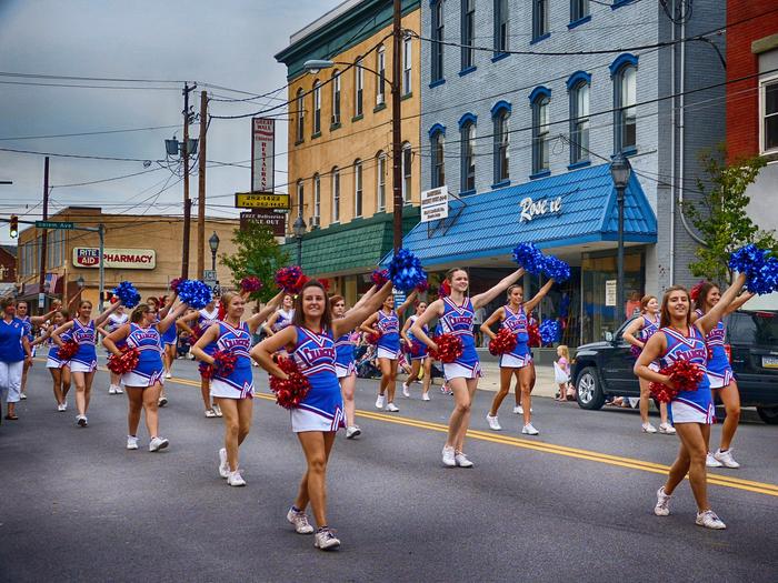 A group of approximately 20 cheerleaders in blue and white uniforms in parade formation walking down a streetThe Pioneer Nights parade will kick off around 6pm