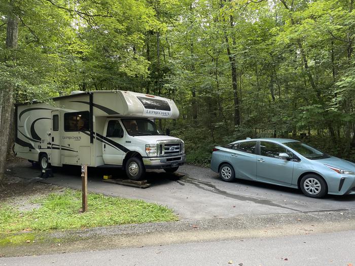 A blacktop surface with a parked RV and blue car.C-16 has a fire ring and picnic table.