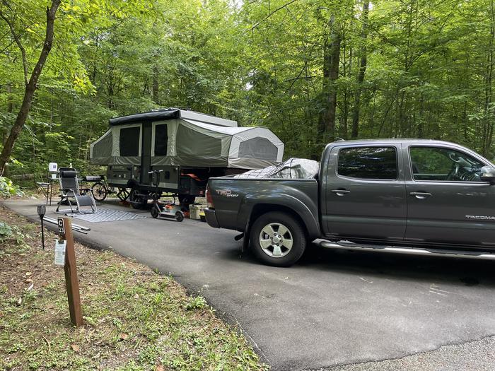 A blacktop surface with a parked camper and a grey truck. C-23 has a fire ring and picnic table.