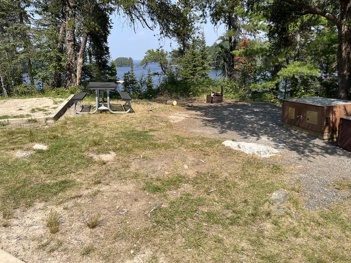 View looking out from campsite core area of the bear lockers, picnic table, and fire ring with water in the background.View looking out from campsite core