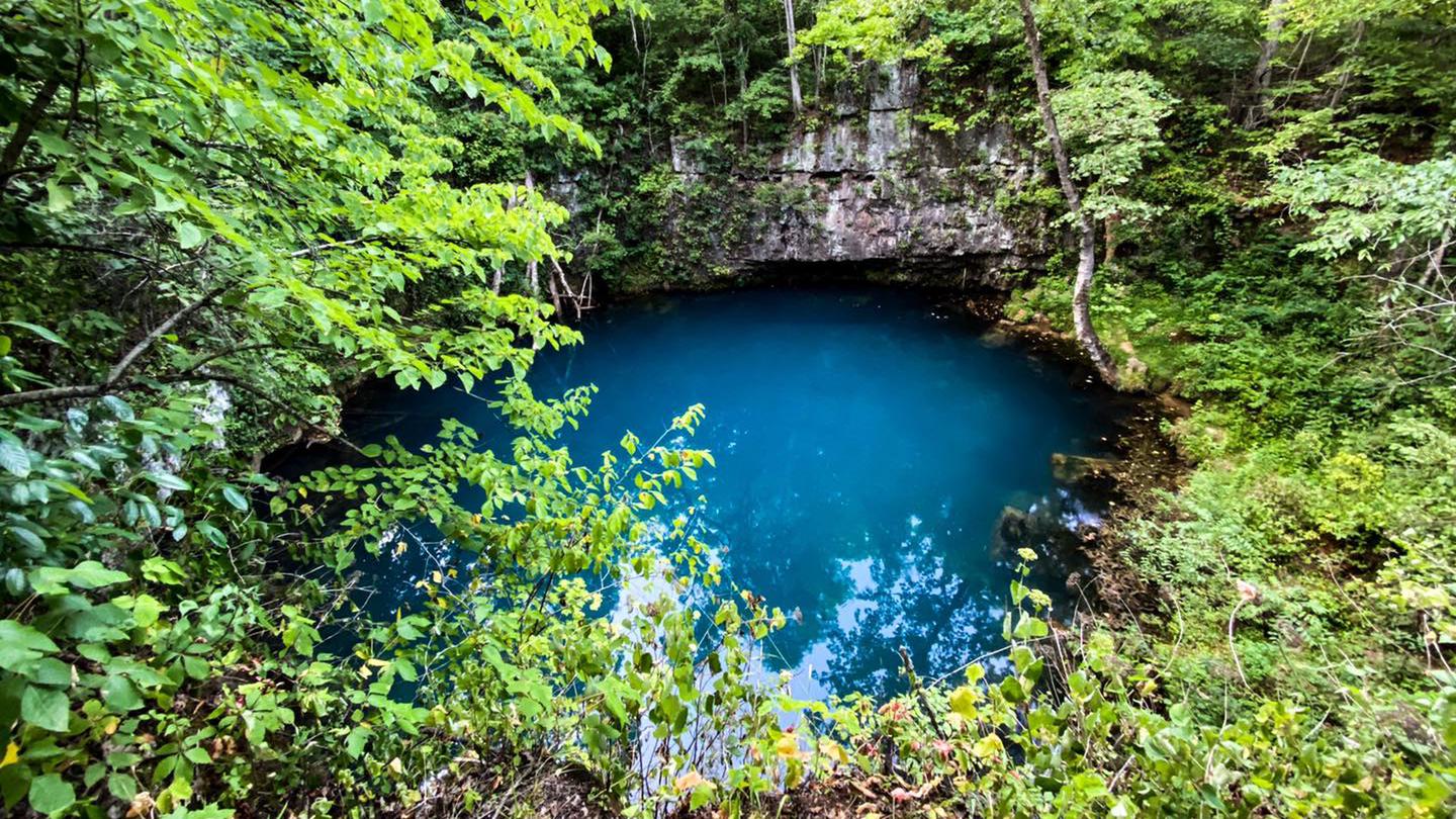 The bright blue water of Round Spring surrounded by greenery