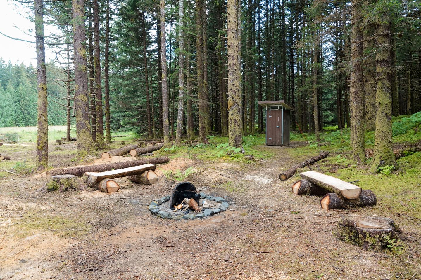 a fire ring with log benches and outhouse in backgroundFire pit area and outhouse