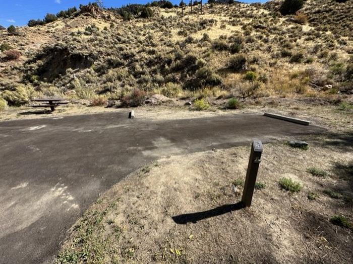 Campsite 8: driveway, picnic table, and firepit. Set in sagebrush and trees.