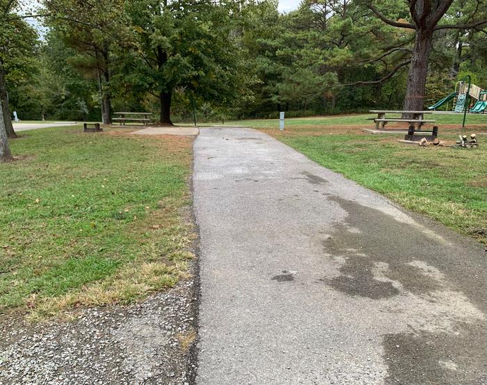 This site has a tree line at the rear of the site  with the picnic table and fire pit located on the left side of the paved parking/camping pad and the hookups are located to the right of the pad. 