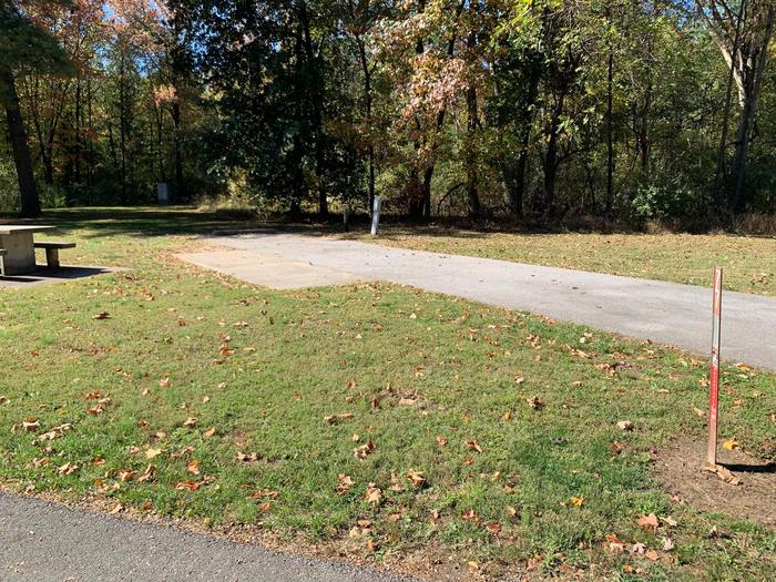 This site has a picnic table and fire pit to the left side of the paved parking/camping pad. Hookups are to the right of the pad. There is a tree line to the rear of the pad. 