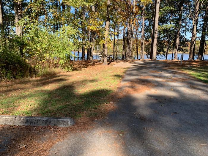 This site has a picnic table and fire pit to the left side of the paved parking/camping pad. The hookups are on the right side of the pad. There is a tree line on the right side of the pad also. 