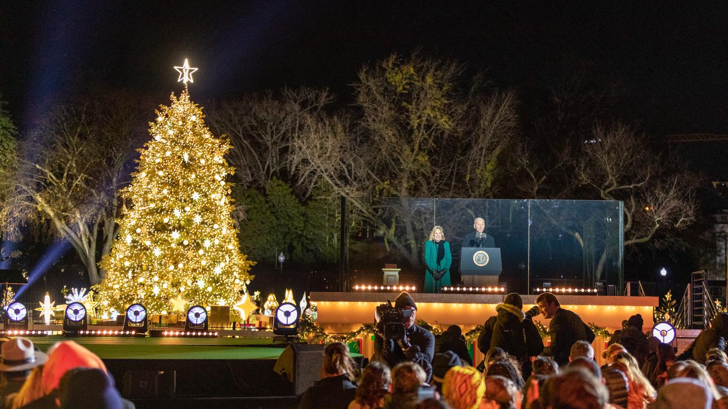 President Biden and the First Lady stand behind glass at a podium President Joe Biden and First Lady Dr. Jill Biden deliver a holiday message at the 2022 National Christmas Tree Lighting
