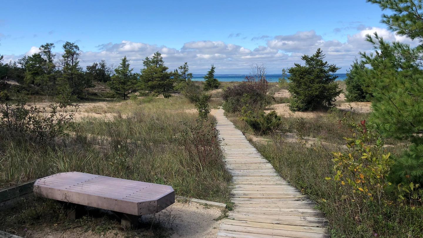 DH Day beach boardwalkA wooden bench sits next to a boardwalk leading to Lake Michigan in the distance.