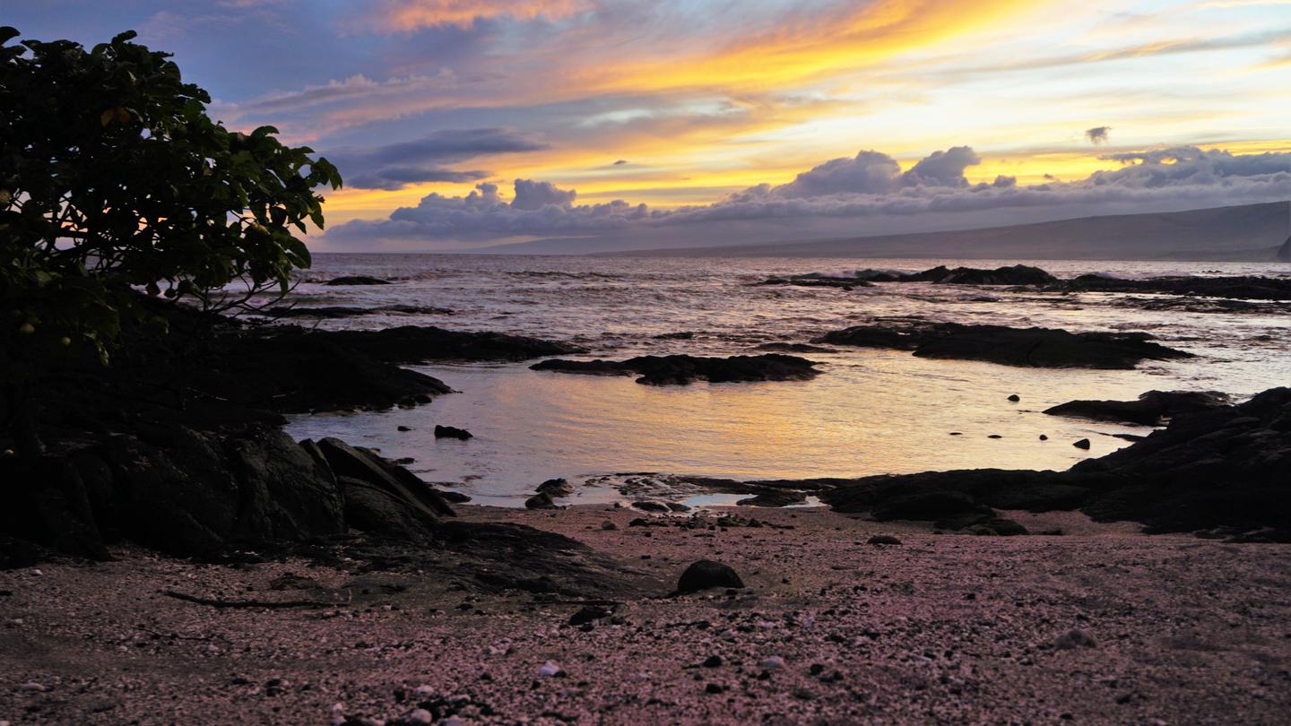 Keauhou shoreline at Sunset. Tide pools in the foreground and an orange/yellow sky at the top of the frameKeauhou at Sunset
