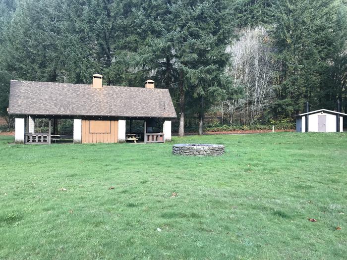 Campsite within meadow landscape, including large stone fire pit, picnic shelter, paved parking, and restroom facilities.River Edge group campground. Includes large picnic shelter, large stone fire pit, large paved parking lot, and restroom facilities.