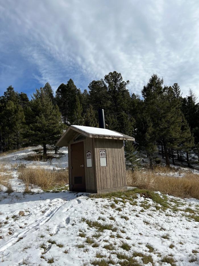 Concrete outhouse surrounded by green trees and snowOuthouse