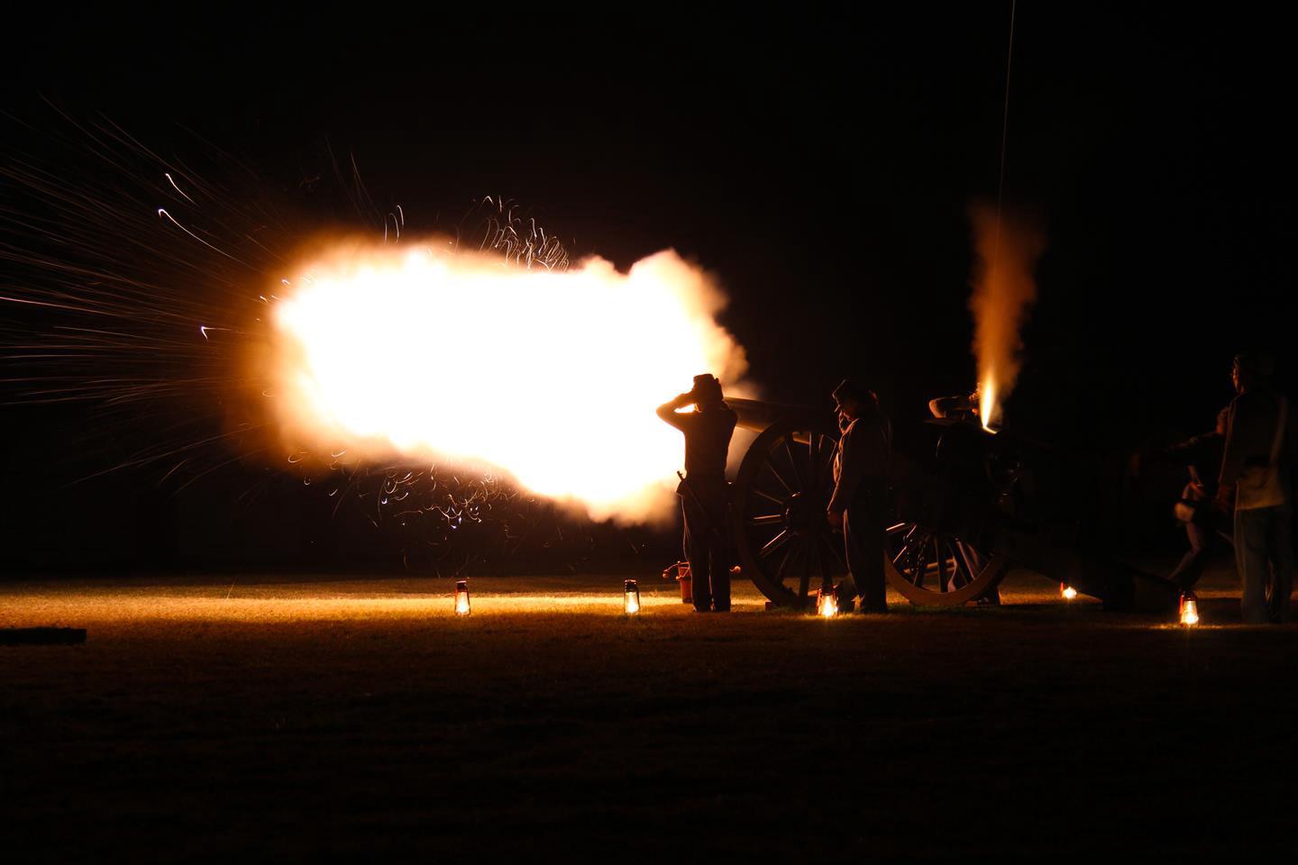 Two individuals standing near a cannon, blasting in the dark Candle Lantern Cannon Firing