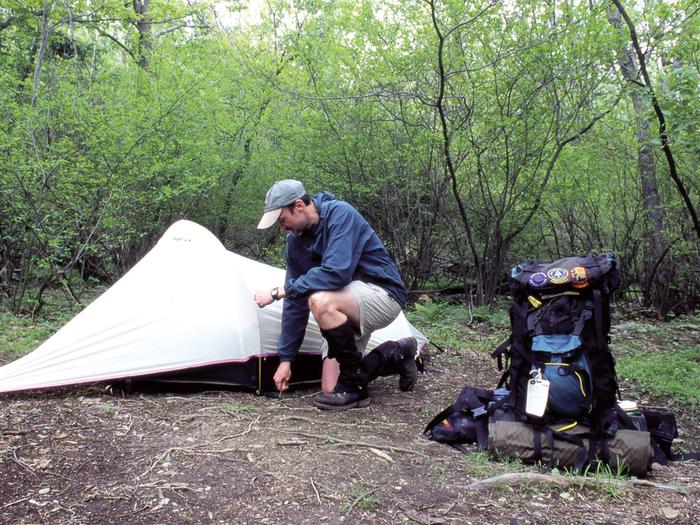 Person setting up tent with backpack nearby.Backcountry camper setting up tent.