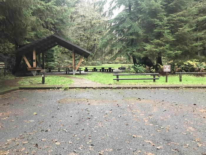 Large group campsite within forested grassy landscape. Includes grass field. Includes multiple paved parking spots. Sign says no day use parking. Water spigot present. Includes large gazebo consisting of multiple picnic benches. Includes large firepit.Group site within Cape Perpetua Campground. Includes multiple paved parking spots. Sign says no day use parking. Water spigot present. Includes large gazebo consisting of multiple picnic benches. Includes large firepit.