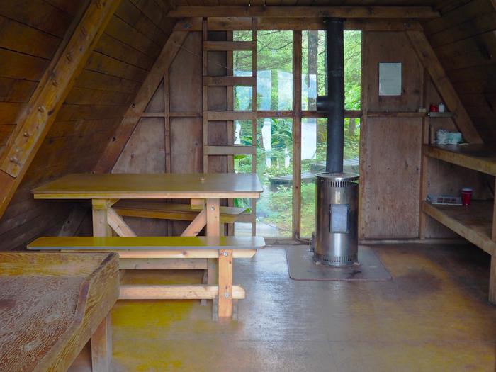Berg Bay Cabin interior with window, wooden ladder, table and oil stove.Berg Bay cabin interior