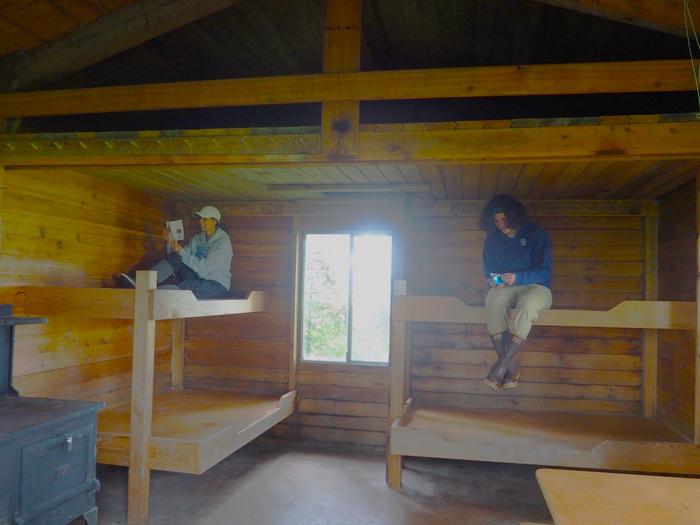 Gut Island Cabin 1 interior with two people reading books on the top of wooden bunksGut Island Cabin 1 interior