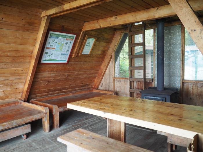 Interior of wood cabin showing 2 wood bunks, table, stove and ladder up to loftInterior of Mallard Slough Cabin