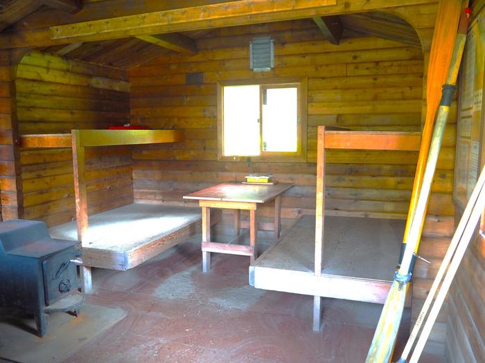 Marten Lake Cabin interior showing 4 wood bunkbeds, small table and stove with oars leaning against wallMarten Lake Cabin interior