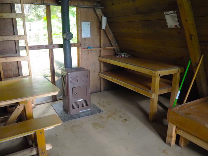 Mount Flemer Cabin interior showing wooden table and shelves with stoveMount Flemer Cabin interior