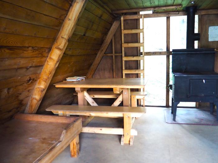 Mount Rynda Cabin interior showing wood table and bed with stove and ladder to loftMount Rynda Cabin interior