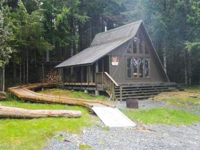 Outside of Steamer Bay Cabin with woodshed, showing ramp to cabin from gravel.Exterior of the cabin with ramp and woodshed