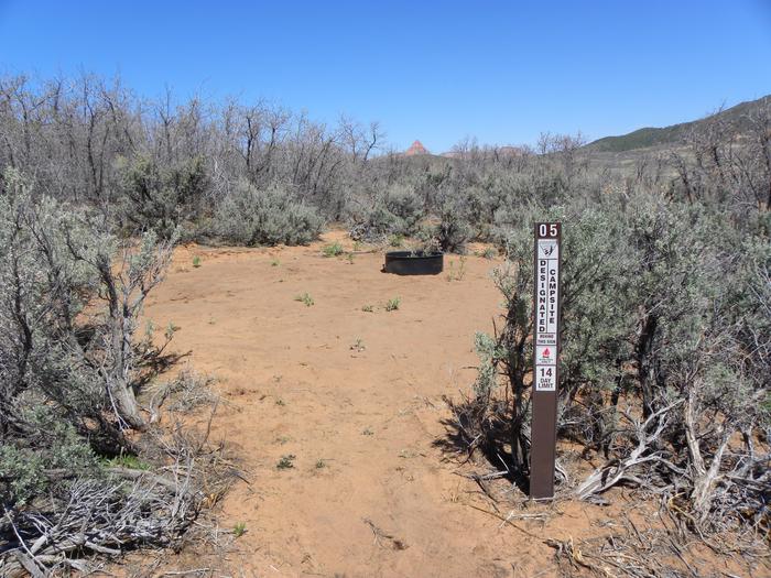 Lambs Knoll Designated Dispersed Camping AreaCampsite with brown, numbered placard (#5) and a metal campfire ring in sandy soil, surrounded by a dense perimeter of sagebrush and shrub oak. 
