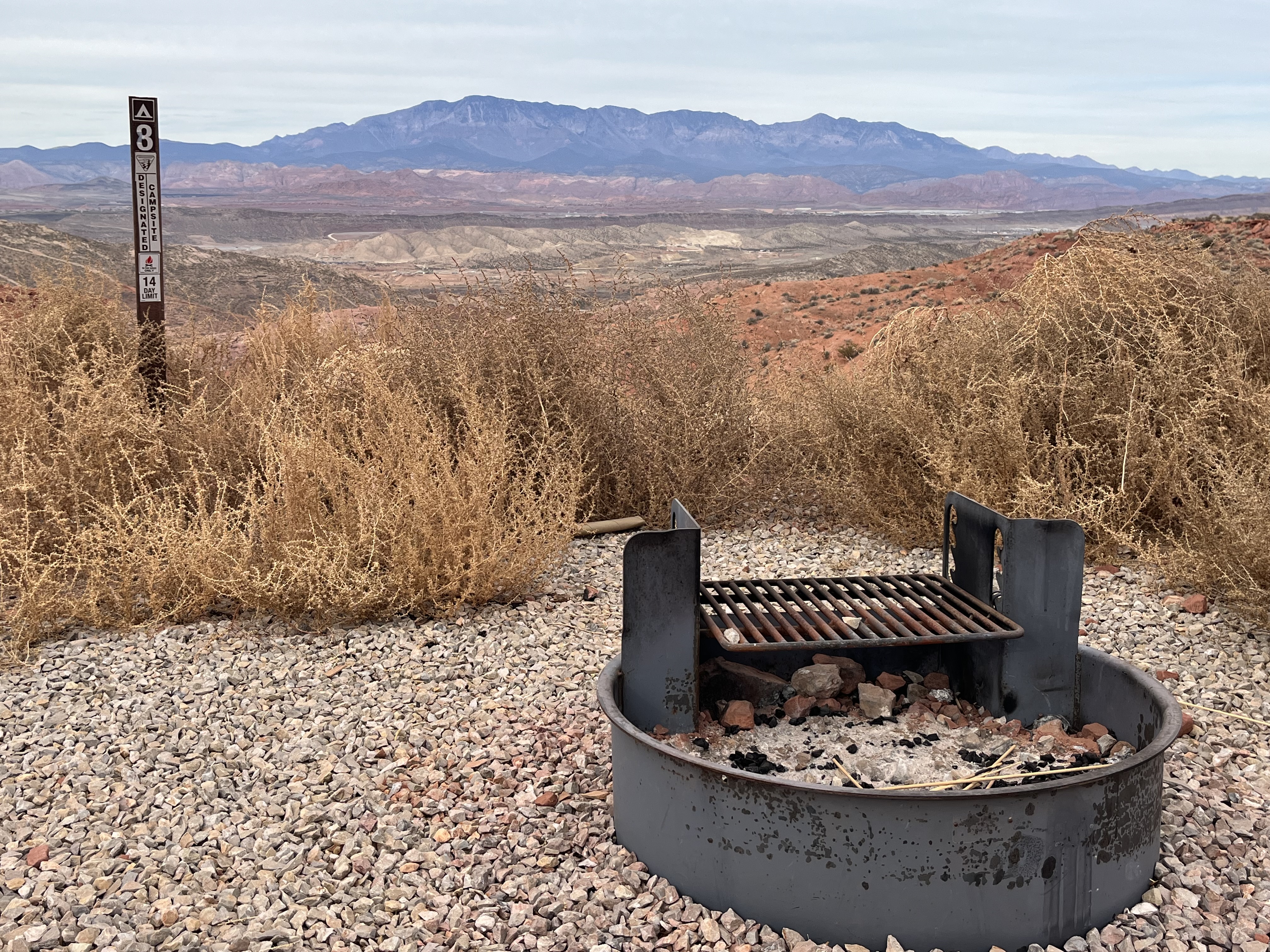 Graveled campsite against a backdrop of rolling red dirt hills and the Pine Valley Mountains. 