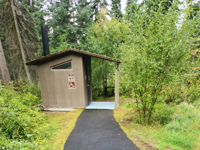 A photo of a Lake Alva Campground vault toilet. There is a paved, accessible walkway. 