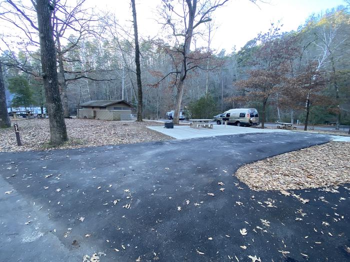 Black asphalt creates an RV parking pad; a picnic table, fire ring, and grill are fully paved. Campsite 17, a view from the road.