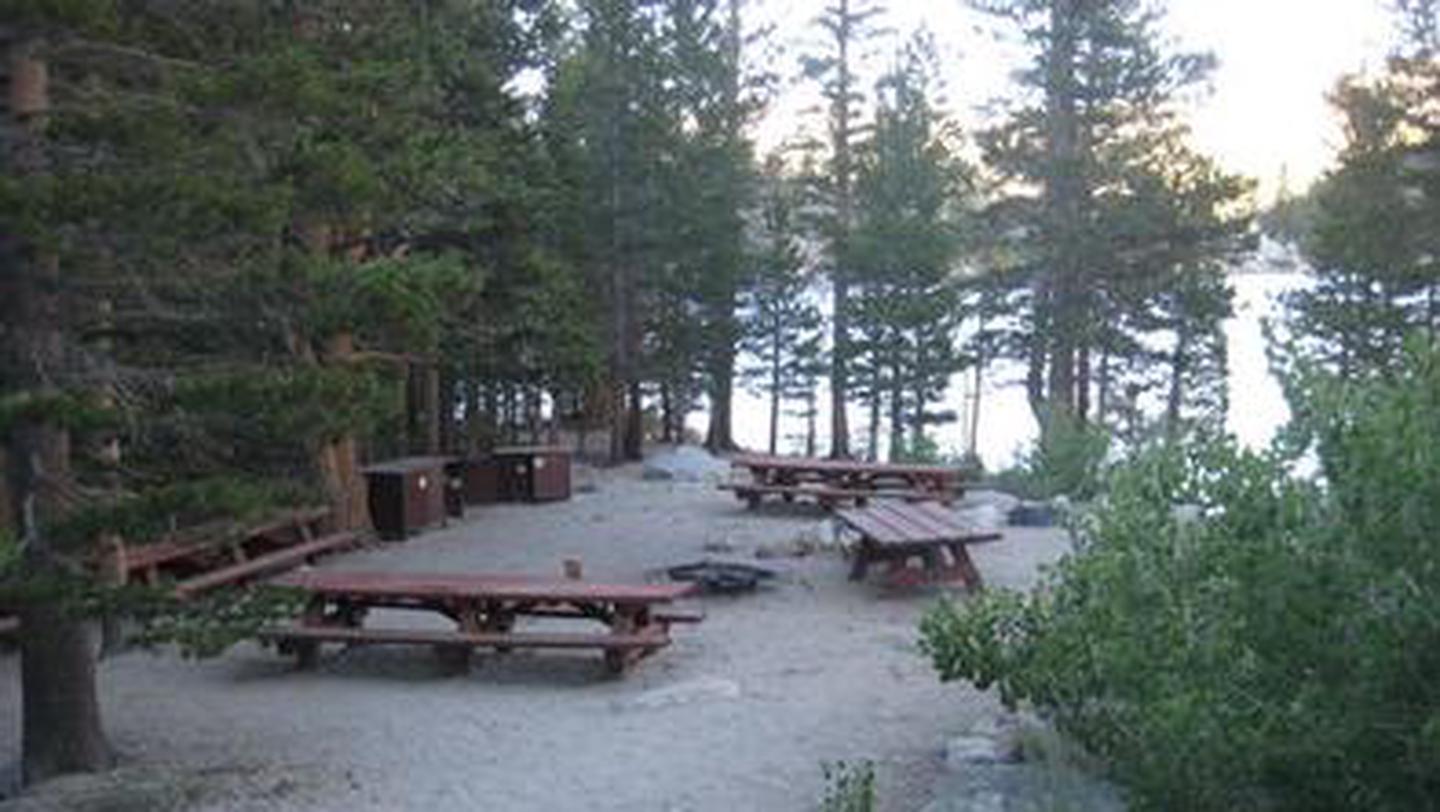Several picnic tables around a fire ring on a cliff near a lakeRock Creek Lake Group Camp