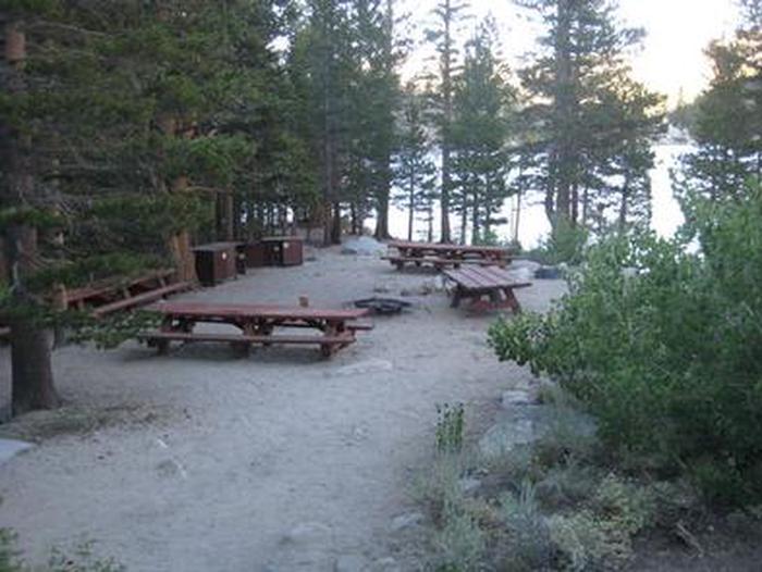 Several picnic tables around a fire ring on a cliff near a lakeRock Creek Lake Group Camp