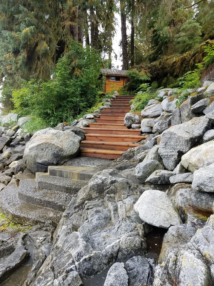 Stone and wooden steps leading up to an outhouse.Steps to the trailhead