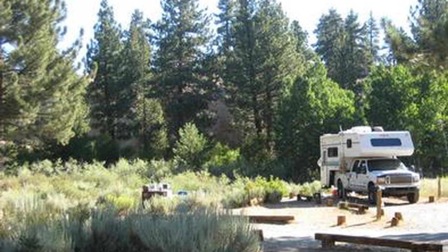A pickup truck with an attached camper parked at a dirt campsiteTuff Campground