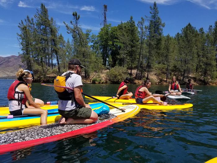 A group of paddleboarders relaxing while listening to a ranger at one of several tour stops.Whiskeytown Paddleboarding