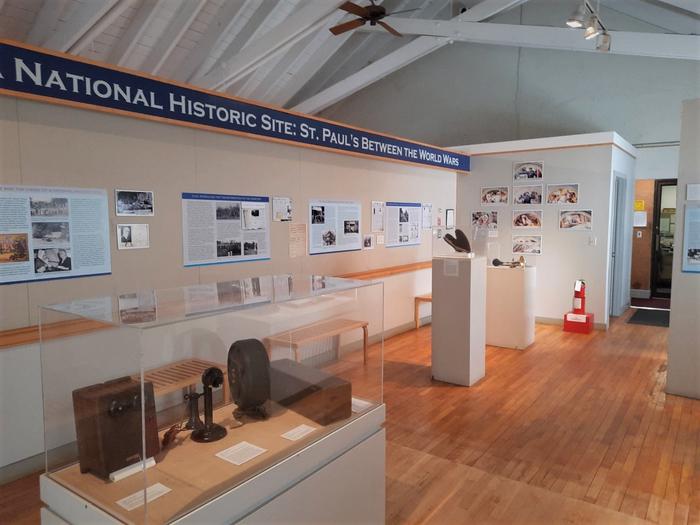 Exhibition space in a museum, with wall panels and display cases with artifacts. Display space for the current feature exhibition in the museum, "The Emergence of a National Historic Site: St. Paul's Between the world Wars". 