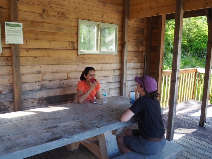 Two people eating lunch and a wooden picnic tableVisitors enjoying lunch outdoors at Deep Bay Cabin