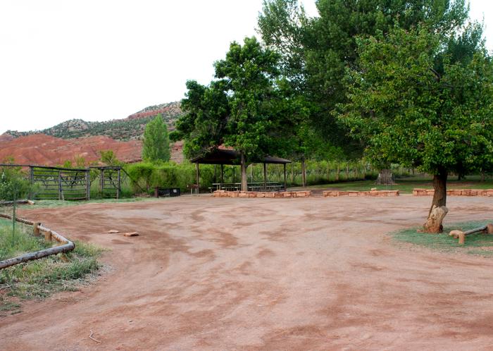 A dirt parking area. A pavilion is in the background and a few trees are next to it. Entrance and Parking Area