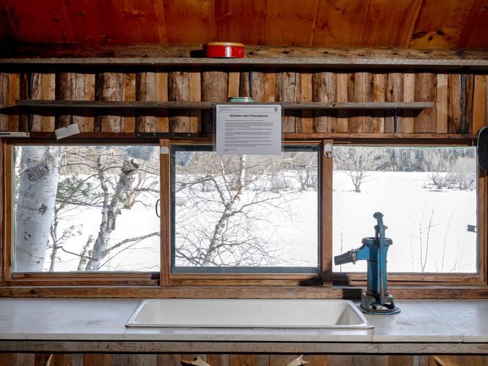 A small panoramic length window brings a view of the winter landscape above a sink inside a wood cabin.Enjoy a beautiful view through the kitchen windows. Follow Leave No Trace principles.
