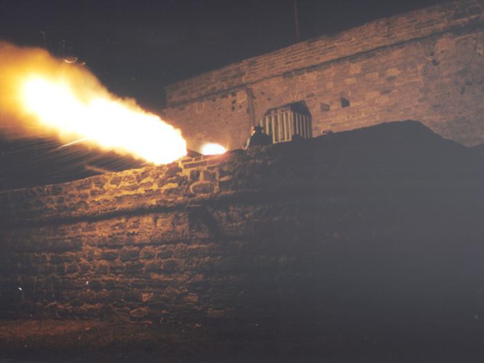 Night view of Coquina fort. Flame Plume out of mouth and vent hole of Replica 6 Pound Iron Cannon. Single Soldier on righthand side of 6 Pound Cannon, wearing Spanish Blue Great Coat with Red cuffs and Black Tricorn Hat with a Red Bow.  Night Firing of Replica 6 Pound Cannon at Fort Matanzas National Monument