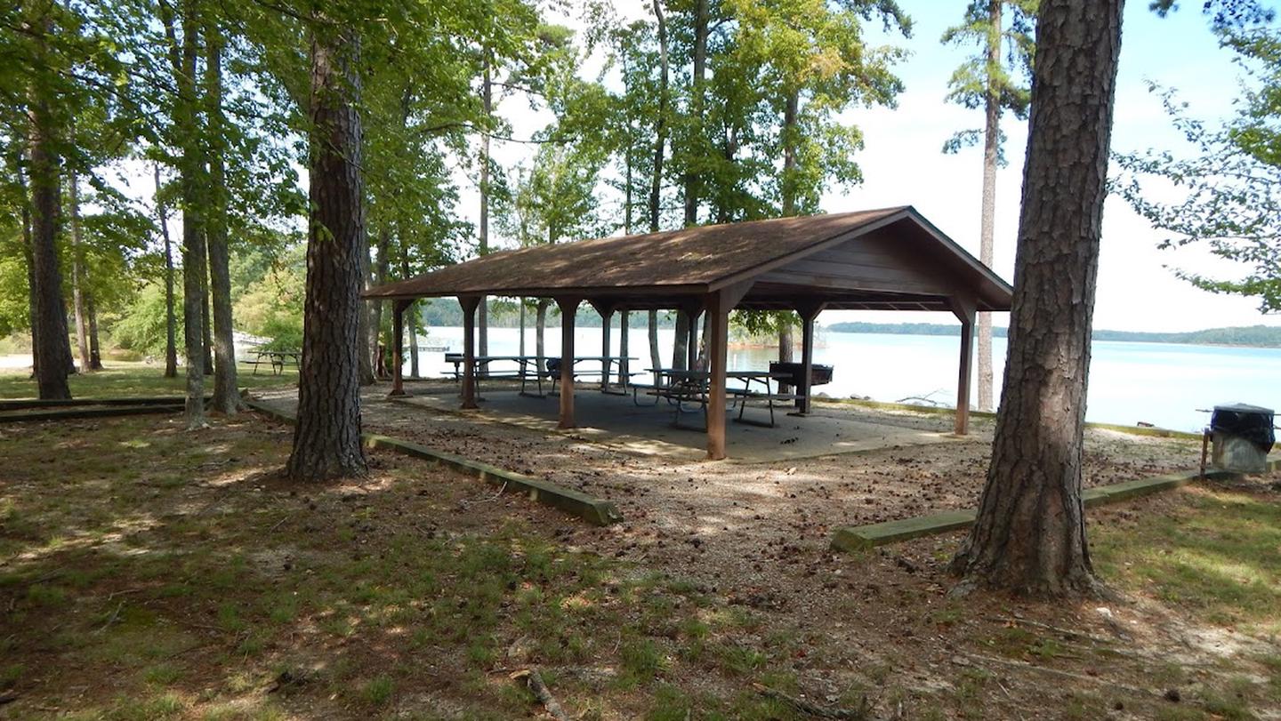 This is a picture of the Ivy Hill Shelter that you can reserve. This is a picture of the Ivy Hill Shelter that is reservable. There are picnic tables under a covered shelter. This area is shaded but has a wonderful view of the lake. There are trash cans located throughout the park. 