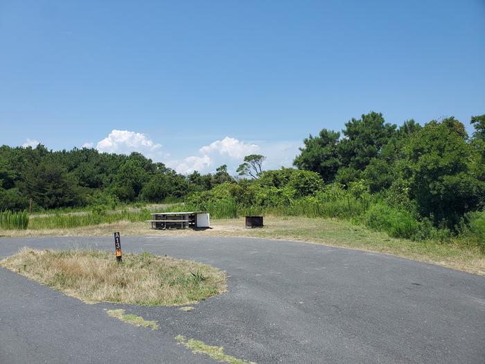 Bayside site A13 in July with a view from the main road.  Image shows the picnic table, fire ring, and site signpost.  Partial view of the pull-through drive-in site.Bayside A13 - July